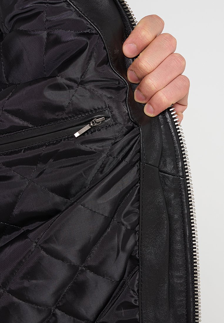 Chaqueta de cuero negra con un forro interior de nylon acolchado; cuenta con un bolsillo con cremallera y herrajes de cremallera plateados en la parte frontal.