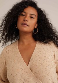 Bež pulover iz pletenine z zavitim dizajnom, ki ima sijoče zlate bleščice, mehko teksturo in globok V-izrez.