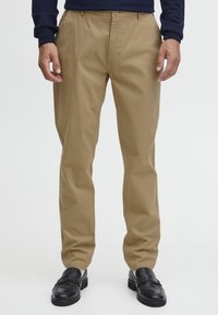 Khaki chinos s ravnim krojem, izrađeni od glatkog materijala, s kopčanjem na dugme i prednjim džepovima. Nošeni s crnim loafers cipelama.