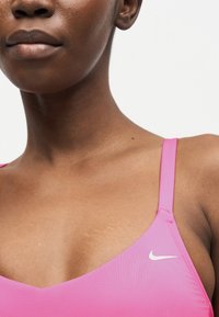 Κοντινό του άνω μέρος του στήθους και του λαιμού ενός ατόμου που φοράει ροζ αθλητικό σουτιέν Nike με λεπτές τιράντες και ορατή υφή δέρματος.