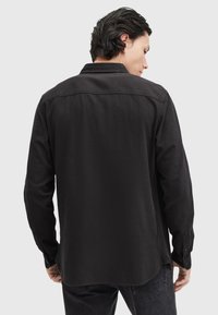 Zwarte longsleeve shirt met een relaxte pasvorm, button-down kraag en een gladde textuur. Bevat een rechte zoom en knoopmanchetten.