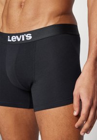 Schwarze Baumwoll-Boxershorts mit einem elastischen Bund, der ein Logo trägt. Enganliegendes Design mit flachen Nähten und einer glatten Textur.