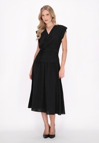 Abito nero con design a fascetta, maniche corte e vita accentuata da una cintura. Tessuto fluido con lunghezza midi, completato da tacchi alti neri.