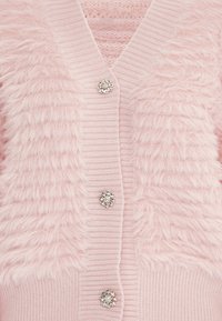 Cardigan rosa con pelliccia artificiale testurizzata sulle spalle, corpo a maglia a coste e cinque bottoni decorativi simili a gioielli nella parte anteriore.