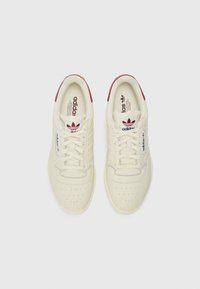 Koorid kreemivärvi Adidas tossud burgundi aktsentidega, siledast nahast ülemine osa, augudega varvas ja klassikaline kolme riba disain. Lood on kaasas.