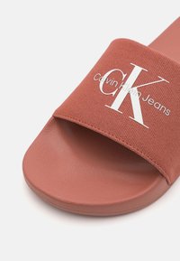 Infradito Calvin Klein Jeans in terracotta con una fascia in tessuto che presenta un logo bianco e una suola in gomma arrotondata e testurizzata.