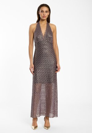 Femme portant une robe dos-nu en crochet lavande, ajustée, avec des talons dorés à bouts pointus, debout devant un fond blanc.