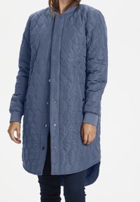 Gepolsterter langer Mantel aus weichem blauen Stoff, mit Druckknopfverschluss, gerippten Ärmelbündchen und einem abgerundeten Saum mit leichtem Schwanz.