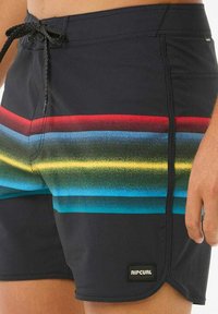 Bañador negro con franjas horizontales en rojo, amarillo, verde y azul. Incluye cinturilla con cordón y etiqueta de marca.