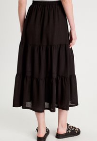 Falda maxi de varias capas en negro, hecha de un tejido ligero, con cintura elástica y una silueta fluida con una textura suave.