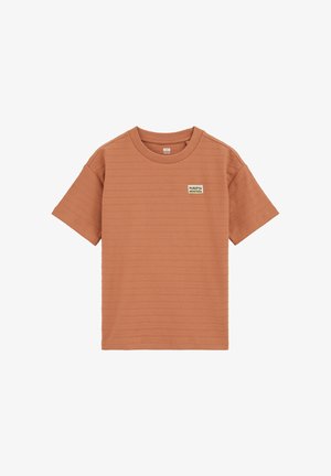 Rövid ujjú, égett narancssárga ing, texturált mintával, kerek nyakkivágással és egy kis "PUERTO MONTAÑA" felirattal a bal mellrészen.