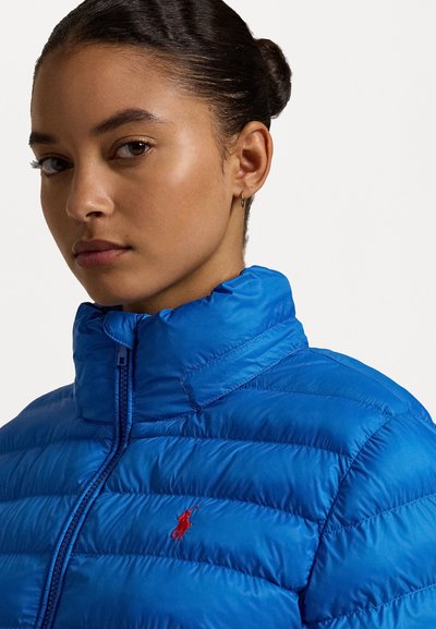 Blauwe pufferjack met hoge kraag, voorzien van horizontale stiksels, ritssluiting en een klein rood logo aan de linkerkant.