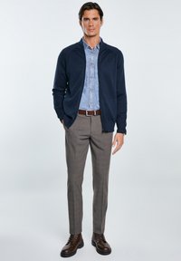 Námornícky zipsový cardigan cez svetlomodrú košeľu z chambray, skombinované so šedými nohavicami s kockovaným vzorom a hnedými šnurovacími čižmami.