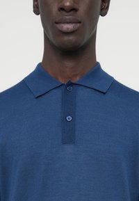 Polo bleu marine avec une texture côtelée, petit col et patte à deux boutons ; présente un design uni sans motifs ni accents.