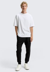Camiseta blanca de manga corta combinada con pantalones negros y zapatillas blancas. Tejido suave, ajuste relajado y diseño de cuello redondo. Estilo minimalista.