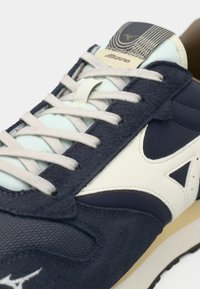 Marineblå ruskinds- og mesh-sneakers med hvide læderdetaljer, lyseblå tunge og beige sål. Har flade snørebånd og logo-detalje.