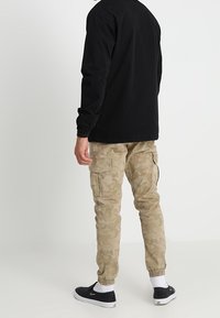 Czarna, lekka kurtka z wysokim kołnierzem, zestawiona z beżowymi spodniami cargo w kamuflażu z elastycznymi mankietami i bocznymi kieszeniami. Czarne trampki.