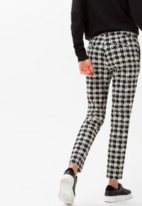 Pantalon à motif pied-de-poule en noir et blanc, coupe slim, taille mi-haute, associé à des baskets noires.