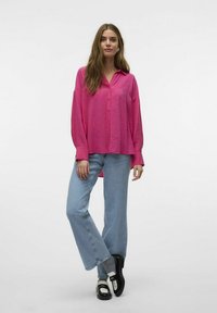 Fuchsia langærmet skjorte med knaplukning og afslappet pasform, parret med lyseblå vide jeans og sorte sko med hvide accenter.