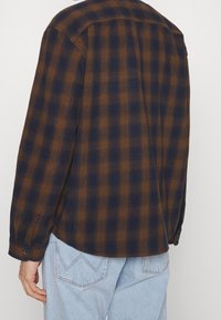 Rutigt flanellskjorta i marinblått och brunt, lång ärm, knapport på ärmarna, och avslappnad passform med rundad nederkant. Texturerad tyg, avslappnad design.