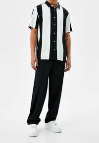 Camicetta a maniche corte con audaci righe verticali bianche e nere, con bottoni frontali, abbinata a pantaloni neri a vestibilità comoda e sneakers bianche.