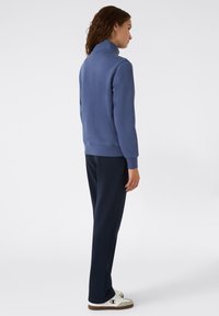 Pullover in pile blu con colletto alto, abbinato a pantaloni della tuta blu navy. Il tessuto è morbido, con maniche lunghe e una vestibilità comoda.
