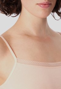 Light pink camisole with thin straps and lace trim along the neckline. Smooth, stretchy fabric with a soft texture, highlighting skin tones.