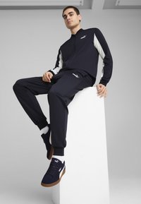 Marine trainingspak met witte accenten, een ritsjack en elastische manchetten. Gecombineerd met marine sneakers met een gumrubberen zool en logo.
