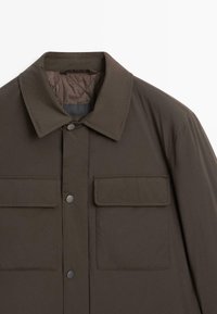 Mörkbrun jacka med krage, tryckknappar och två bröstfickor med lock. Slät yta och minimal sömnad.