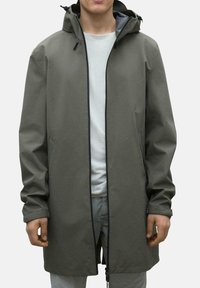 Chaqueta de lluvia color caqui con una silueta larga, que presenta un cierre de cremallera, capucha con cordón, bolsillos laterales y puños elásticos. Textura suave.