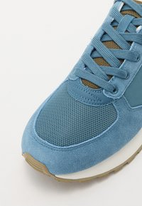 Zapatillas de red y gamuza azul con parte superior texturizada, cierre con cordones, lengüeta acolchada y suela de goma con un acento en color tostado.