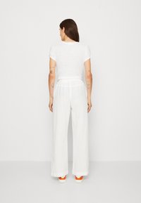 Haut blanc à manches courtes associé à un pantalon blanc ample. La tenue présente une silhouette décontractée et est fabriquée en tissu léger.