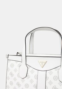Borsa a tracolla bianca in pelle con un design decorato, bordi neri, doppi manici e un accento dorato a forma di triangolo sul davanti.