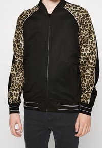 Giubbotto bomber nero con maniche in stampa leopardata, polsini e colletto a coste, chiusura con zip e tasche laterali. Tessuto testurizzato con righe bianche.