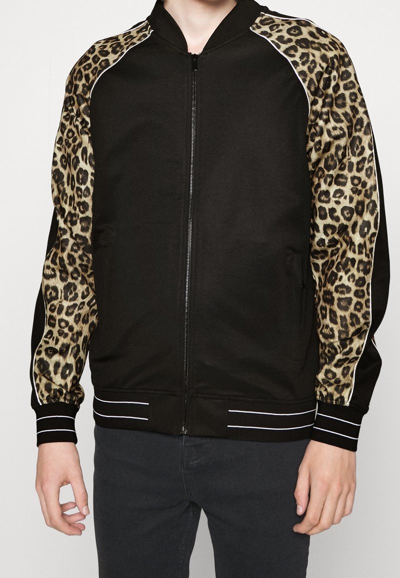Giubbotto bomber nero con maniche in stampa leopardata, polsini e colletto a coste, chiusura con zip e tasche laterali. Tessuto testurizzato con righe bianche.