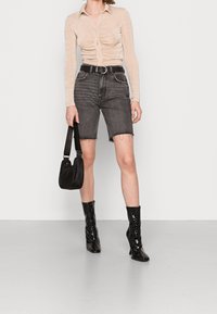 Långärmad beige topp med rynkad framsida, mörka denim bermudashorts, svart handväska och glänsande svarta ankelboots med spetsiga tår.