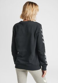 Sudadera negra de manga larga, con franjas diagonales grises en la manga izquierda. Textura suave y puños acanalados en el dobladillo y el cuello.