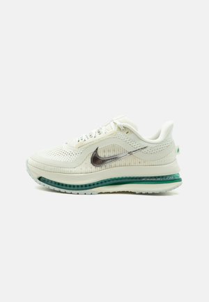 Nike løbesko i cremefarve med mesh-overdel, sølv Swoosh-logo og synlig grøn air-cushion sål, vist fra siden.
