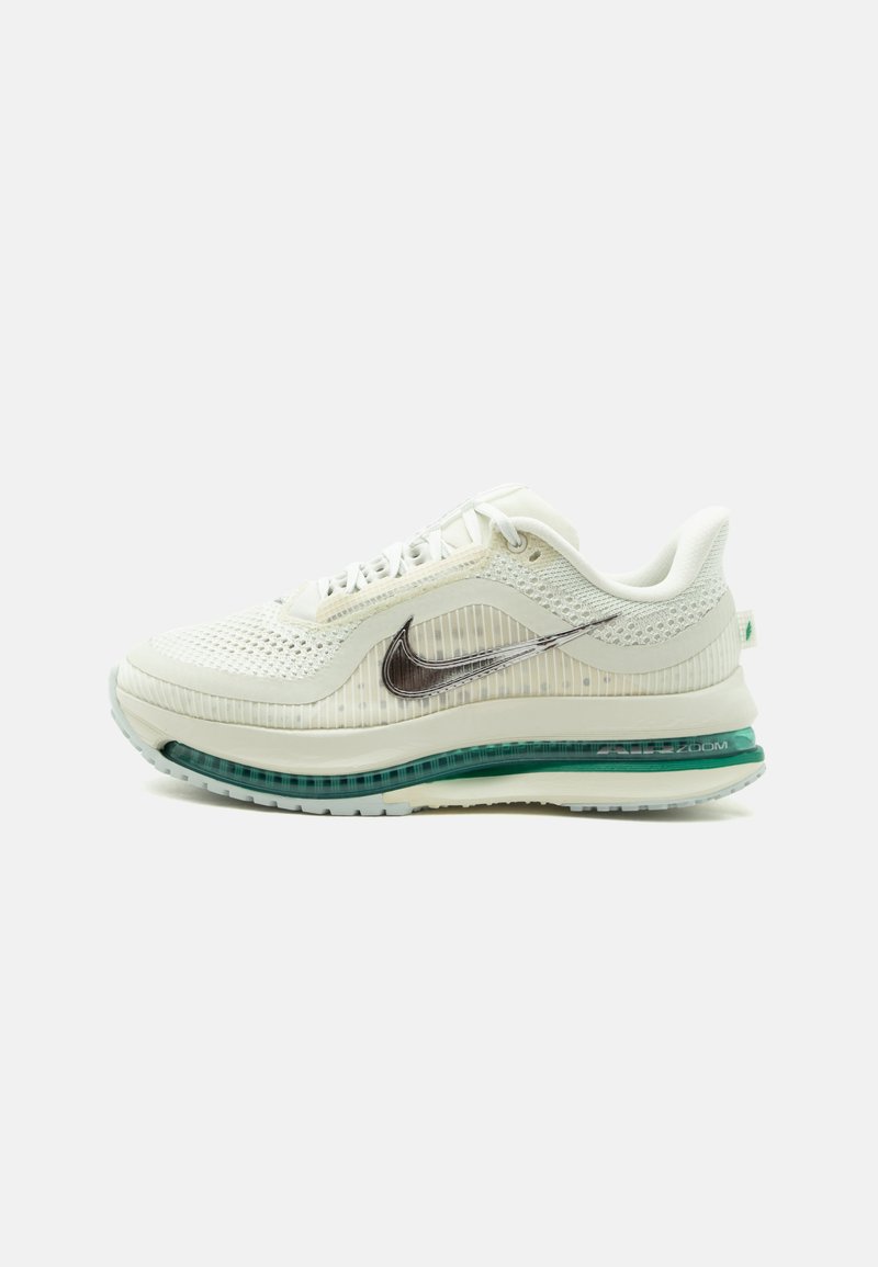 Αθλητικό παπούτσι Nike σε κρεμ απόχρωση με επάνω μέρος από δίχτυ, ασημί λογότυπο Swoosh και ορατή πράσινη σόλα με αερόσολα, εμφανίζεται από το πλάι.