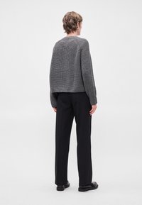 Γκρι πλεκτό πουλόβερ με τετράγωνη εφαρμογή, ριμπ ύφανση και μακριά μανίκια, φορεμένο με μαύρη παντελόνι και παπούτσια. Απλός και μοντέρνος σχεδιασμός.