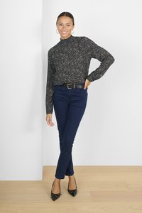 Tumesinine slim-fit teksad musta ja kuldse mustriga pikakäiselise pluusiga ning mustade terava nina kontsakingadega. Kuldsetest rõngastest kõrvarõngad. Minimalistlik taust.