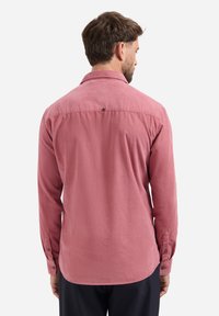 Langsleeve, knoop-up overhemd in stof met een verdoofd rozenkleurtje, met een knoop aan de achterzijde van de kraag en een gevormde zoom. Soepele textuur met een subtiele afwerking.