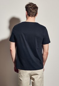 Námořnická modrá tričko s krátkým rukávem vyrobené z bavlny, s kulatým výstřihem a hladkým povrchem, viděné zezadu.