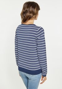Maglione a righe blu navy e bianche con maniche lunghe, scollatura rotonda e un motivo a maglia testurizzato. Indossato con jeans di un blu chiaro.
