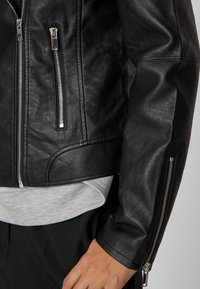 Black leather jacket featuring silver zippers, cropped design, and textured finish. Includes zippers at the sleeves and a layered look.