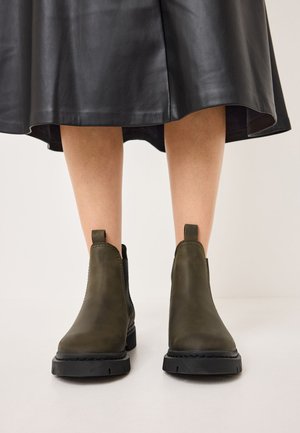 Olive-green leather ankle boots with a smooth texture, black rubber soles, and vertical elastic side panels. Short pull tabs at the back.