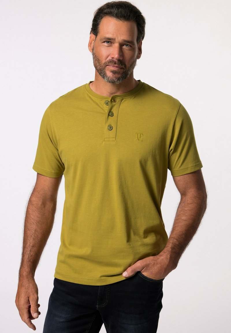 Maglietta henley a maniche corte color verde oliva con patta a tre bottoni e un delicato logo. Tessuto morbido con una trama liscia.