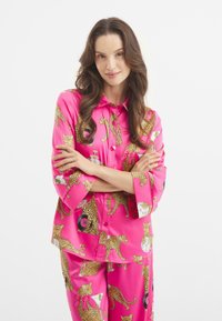 Růžový saténový pyžamový set se leopardími potisky, zvířecími motivy a hravými vzory. Obsahuje halenku s límečkem na knoflíky a odpovídající kalhoty.