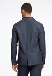 Mörkblå skräddarsydd kavaj med slagkrage, texturerad tyg, enkel bakslits och knäppte ärmar. Enkel och strukturerad design.