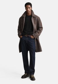 Bruine geruite wollen jas over een zwart shirt, gecombineerd met donkerblauwe jeans en bruine veterlaarzen, met een klassieke pasvorm en een textuurrijke stof.